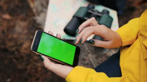 Close up van dames hand schuiven en zoomen op het scherm van de zwarte slimme telefoon in het forest. kaart, verrekijker en rugzak op de onscherpe achtergrond. Groen scherm. Chromakey. Buiten — Stockvideo