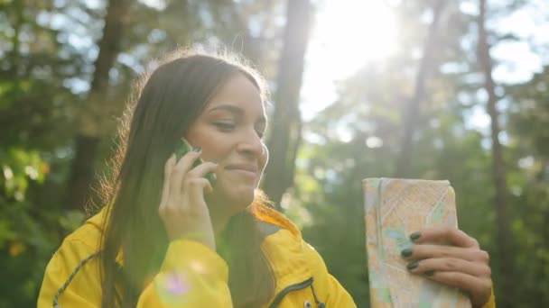 Portrét mladé krásné ženy ve žlutém plášti mluví její inteligentního telefonu v lese v sulight. Zblízka. Vně — Stock video