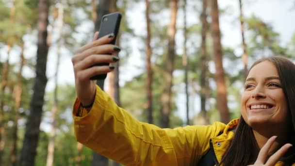 Zbliżenie ładny uśmiechnął się młoda kobieta co selfie na inteligentny telefon i pokazuje gesty w lesie. Portret. Na zewnątrz — Wideo stockowe