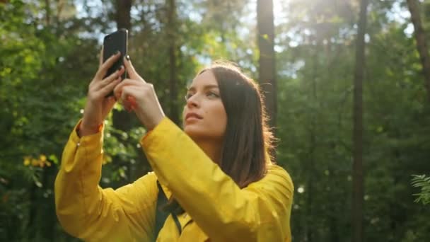 Portrétní snímek mladé krásné ženy fotografování přírody na černé smartphone, zatímco pěší turistika v lese. Slunečný den. Vně — Stock video
