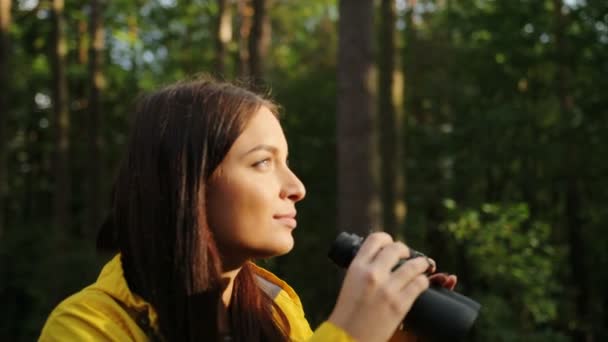 Primo piano della giovane donna affascinante sorridente e guardando nel binocolo nella foresta sorprendente. Giornata di sole. All'aperto. Ritratto — Video Stock