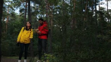 Genç sportif kadın ve adam sırt çantaları rota harita ve yeşil ormanda gülümseyen bir yardımı ile arıyorum. Getting kayıp. Dışarıda