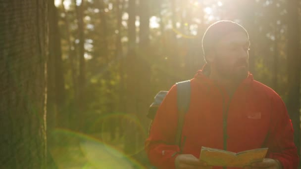 Young sporty man hiker with backpack looking for the way back on the map in the nice green forest. Getting lost. Outdoor. Portrait shot — Stock Video