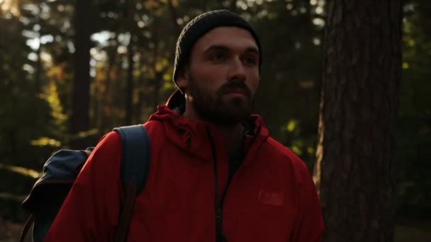 Primer plano del joven guapo con una mochila caminando por el bosque y sonriendo. temprano en la mañana. Al aire libre. Retrato — Vídeos de Stock