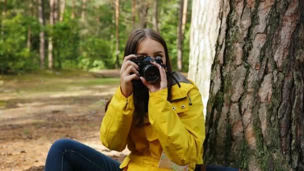 Крупним планом молода чарівна жінка сидить на землі і фотографує природу на старовинній камері в зеленому лісі навколо неї. Зовні. Портрет знятий — стокове відео
