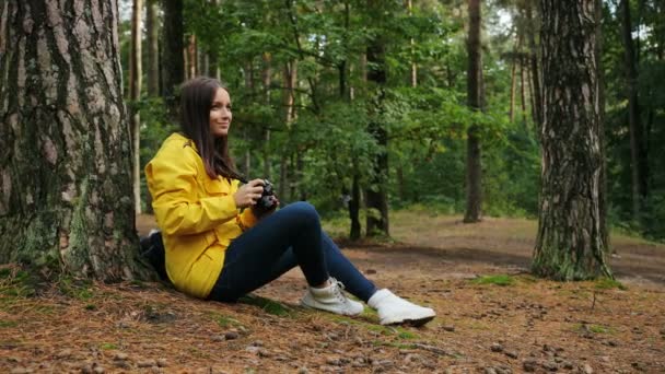 Donna sportiva abbraccio da sola nel bosco, seduta a terra e scattare foto della natura sulla macchina fotografica d'epoca. All'aperto . — Video Stock