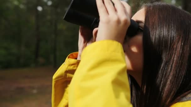 关闭的年轻迷人的黑发妇女看着望远镜在森林里。户外。肖像 — 图库视频影像