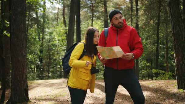 年轻的运动的游客夫妇在五颜六色的大衣和背包站在森林里 看着地图寻找出路 在森林里迷路了 — 图库视频影像