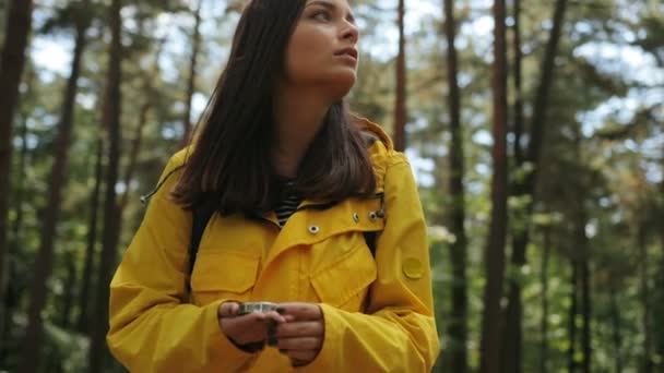 Ung vacker orolig kvinna i gul rock och ryggsäck letar långt tillbaka med hjälp av en kompass mitt i skogen. Jag förlorade. Utomhus — Stockvideo