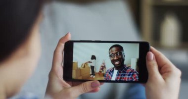 Beyaz bir kadın omzuna ile hangi video sohbet Afrikalı-Amerikalı genç adam ve kız arkadaşı onlar birlikte yeni bir evde yaşamak ile olan siyah bir smartphone üzerinde görüntüleyin. Yakın çekim