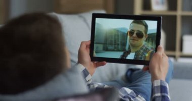 Siyah yakın tablet cihaz adamın elinde bir erkek arkadaşı ile kanepede yalan sırasında konuşan ve web cam.