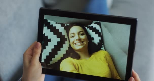 Nahaufnahme weiblicher Hände, die ein Tablet-Gerät halten, während eine charmante lächelnde junge Frau auf dem Bildschirm einen Web-Chat führt. — Stockvideo