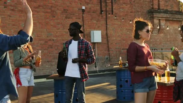 Groupe de jeunes amis bavarder et s'amuser sur la fête sur le toit sur le fond de mur de briques. Un homme qui vient voir ses amis à la fête sur le toit. En plein air. Courses mixtes — Video