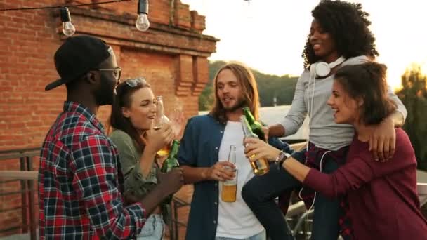 Un grupo de jóvenes amigos bebiendo cerveza y haciendo vítores en la fiesta en la azotea. El fondo de la pared. Afuera. Multi carrera — Vídeos de Stock