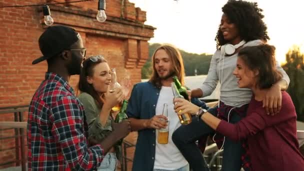 Skupina mladých přátel, popíjeli pivo a dělat na zdraví na střeše party. Zeď na pozadí. Venku. Multi závodil — Stock video