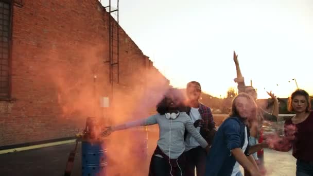 Jeunes gens attrayants marchant et jouant avec la grenade de fumée rose à la fête sur le toit dans l'espace urbain. Le fond du coucher du soleil. Dehors. Multiethnique — Video