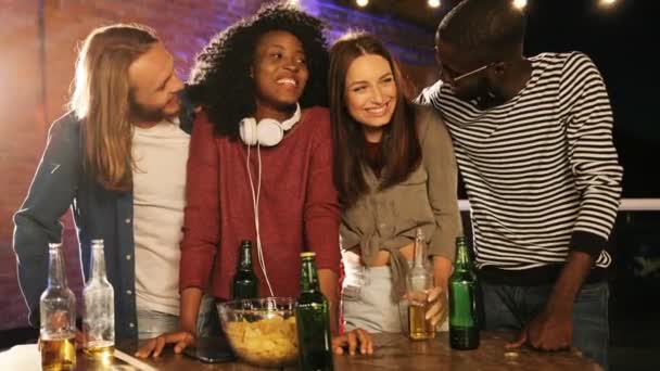 Retrato de jovens multiétnicos em pé à mesa e sorrindo na festa no último piso à noite. O fundo da parede de tijolos. Ao ar livre — Vídeo de Stock