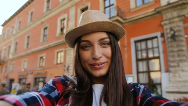 Portrait of pretty girl taking selfie with camera on smartphone. Young woman standing in centre of ancient town on background of beautiful house. — Stock Video