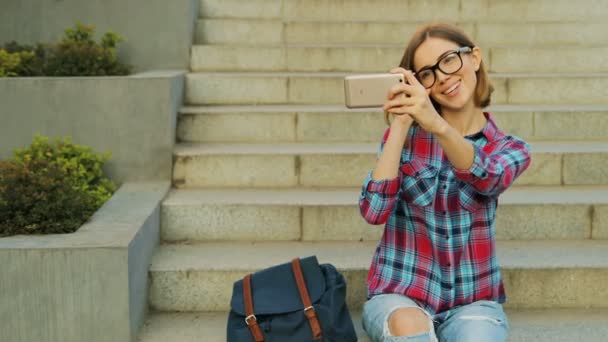 Utomhus livsstil porträtt av leende ung brunett tar en selfie av sig själv i glas på trappan till byggnaden . — Stockvideo