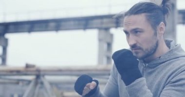 Portre çekici genç adam eğitim toprakları üzerinde çanta kutusuna atılmış eski bitki. Soğuk gri hava. Açık havada