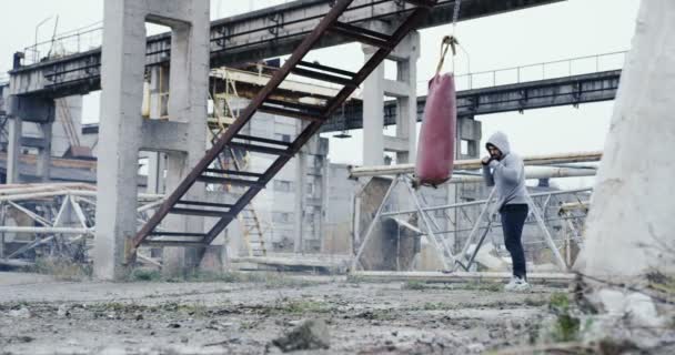 Sportif delikanlı bir başlık boksta soğuk sisli gri sabah terk edilmiş bitki kalıntıları üzerinde kırmızı çanta üzerinde üzerinde mesafeden vurdu. Dışarıda — Stok video