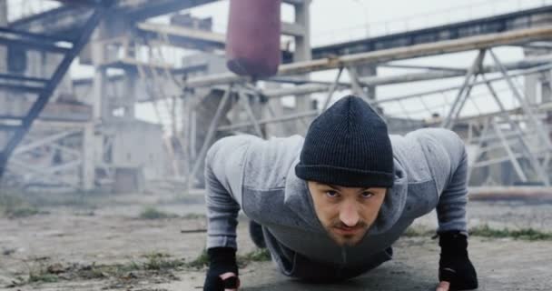 在寒冷多云的早晨, 这位运动的年轻人拳击手在老工厂废墟中做俯卧撑。户外 — 图库视频影像