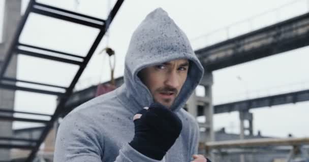 Boxe di fronte alla telecamera sulle rovine del vecchio blocco industriale nel giorno nebbioso freddo. Boxer uomo con cappuccio. Chiudete. Ritratto — Video Stock