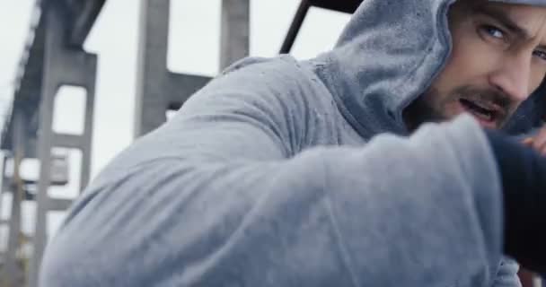 Ritratto del pugile con cappuccio grigio che colpisce la macchina fotografica con il tempo grigio e nebbioso. Chiudete. All'aperto — Video Stock