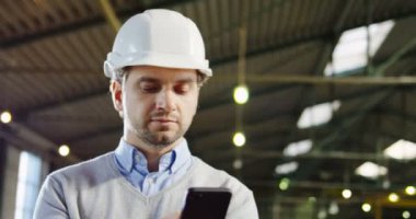 Kayıt ve büyük sanayi tesisinde akıllı telefonuna kaydırma bir kask içinde çekici mühendisi kapatın. Kapalı. Portre vurdu