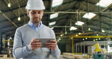 Yakışıklı adam mühendis kaydediyor ve tablet bilgisayarında kaydırma ve büyük fabrika werehouse at etrafa bir kask içinde portre vurdu. Kapalı.