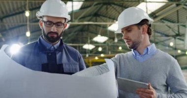 Kask tablet cihaz ve onların proje tartışırken büyük kağıt çizimler ile iki mühendisi. İç büyük fabrikası. Portre vurdu