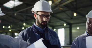Yakın kask üç mühendisleri ile büyük bir konuşmayı ve onların çalışma projesi tartışmaya çizim kağıt. İçinde büyük bir werehouse planlama. Portre vurdu