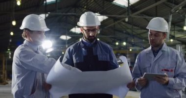 Kask ile bir tablet ve bir konuşmayı ve onların çalışma projesi tartışmaya büyük kağıt çizimler üç mühendislerince portresi. İçinde büyük bir fabrika.
