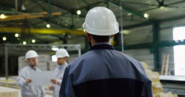 Miğferli yakışıklı fabrika işçisinin arkası mühendislere geliyor ve büyük bir kağıtta gördüklerini çizimlerle tartışıyor. Fabrika alanı. Kapalı.