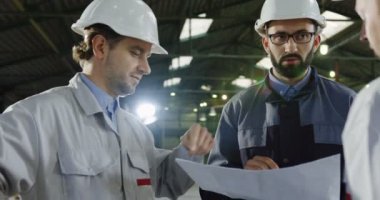 Kask ile büyük üç mühendislerince konuşuyor, tartışıyor ve yeni çalışma projesi kontrol çizimleri kağıt. İçinde büyük bir fabrikada planlama. Portre. Yakın çekim