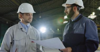 Fabrika işçisi ve kask sallayarak büyük kağıt çizimlerle mühendisi eller ve proje ile ilgili olarak kabul etti. İçinde büyük bir fabrikada. Portre vurdu. Yakın çekim