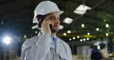 Yakışıklı adam, portre çekim mühendislik akıllı telefonda konuşurken bir kask içinde. Arka planda büyük fabrika Oda.