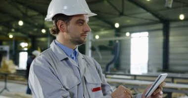 Tablet cihaz üzerinde çalışan bir kask içinde çekici mühendis tarafından gelen portre vurdu. Arka planda büyük fabrika alanı.