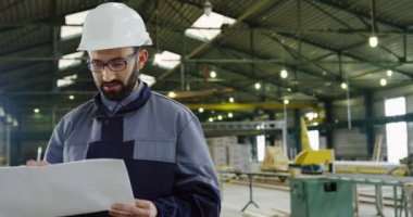 İle büyük çizim kağıtları büyük fabrika alanının ortasında duran ve kameraya gülümseyen fabrikada işçi portresi. Kapalı