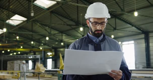 Trabajador de la fábrica de pie con grandes dibujos papeles en el medio del proceso de producción y la comprobación de la obra. Gran instalación industrial. Un retrato. En interiores — Vídeo de stock