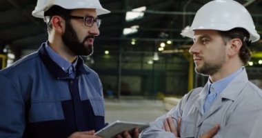 Kask içinde iki fabrika işçileri mühendisleri kendi çalışma projesi tartışmaya bir tablet cihaz ile yakın çekim. İçinde büyük bir fabrika. Portre vurdu
