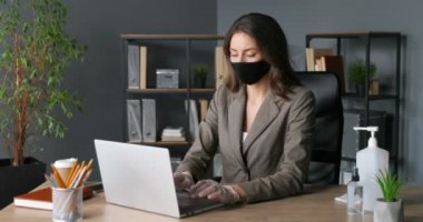 Maskeli, lastik eldivenli, klavyede yazan ve dizüstü bilgisayarda çalışan beyaz bir iş kadını. Güzel bir ofis çalışanı. Koronavirüs pandemik koruması.