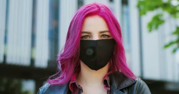 Close up de menina branca muito elegante jovem com cabelo rosa vestindo máscara preta e olhando diretamente para a câmera ao ar livre. Retrato de fêmea extraordinária em proteção respiratória . — Vídeo de Stock