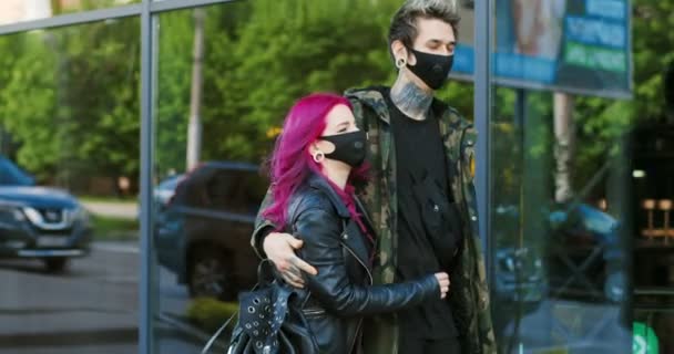 Iloinen valkoihoinen nuori tyylikäs pari hipsters kävely roikkuu kadulla aikana covid-19 pandemia. Kaunis ylimääräinen tyttöystävä vaaleanpunaiset hiukset ja poikaystävä tatuoinnit kävelee naamioissa — kuvapankkivideo