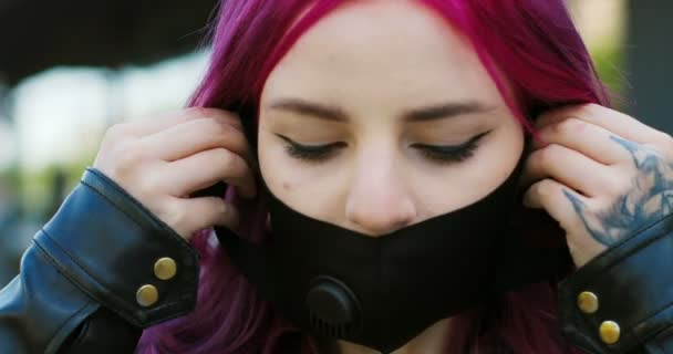 Zbliżenie młodych dość stylowe białej dziewczyny z różowymi włosami noszenie czarnej maski i patrząc na zewnątrz kamery Portret niezwykłej kobiety z jasnym kolorze włosów biorąc na ochronę dróg oddechowych — Wideo stockowe