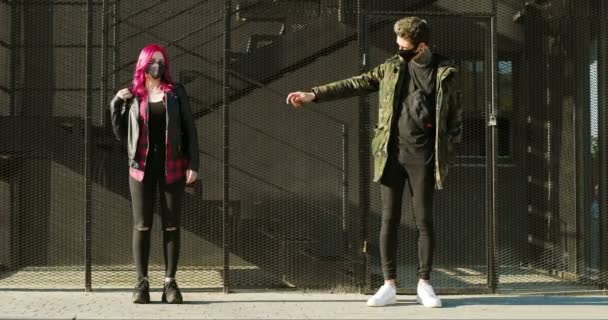 Couple caucasien de hipsters extraordinaires dans des masques gardant la distance sociale et debout avec les bras tendus à l'extérieur. Fille avec des cheveux roses et mec avec des tatouages dans des masques passer du temps ensemble . — Video