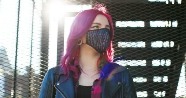 Portrait of stylish beautiful Caucasian girl with pink hair in black mask looking at side at stairs outdoors. Close up of extraordinary woman in respiratory protection during coronavirus lockdown. — Stock Video