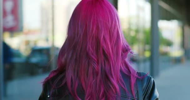 Primer plano de la parte trasera de la joven chica extraordinaria del Cáucaso con el pelo rosa y en máscara negra caminando al aire libre, a continuación, gire a la cámara. Vista trasera de la mujer hipster elegante paseando por la calle y volver atrás . — Vídeo de stock