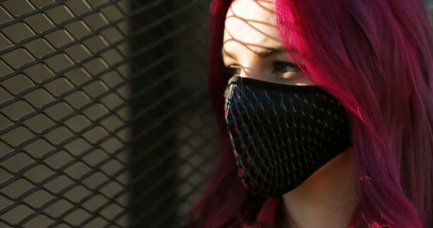 Close up of face of stylish beautiful Caucasian girl with pink hair in black mask looking at side and turning face to camera. Portrait of extraordinary woman in respiratory protection during covid-19. — Stock Video