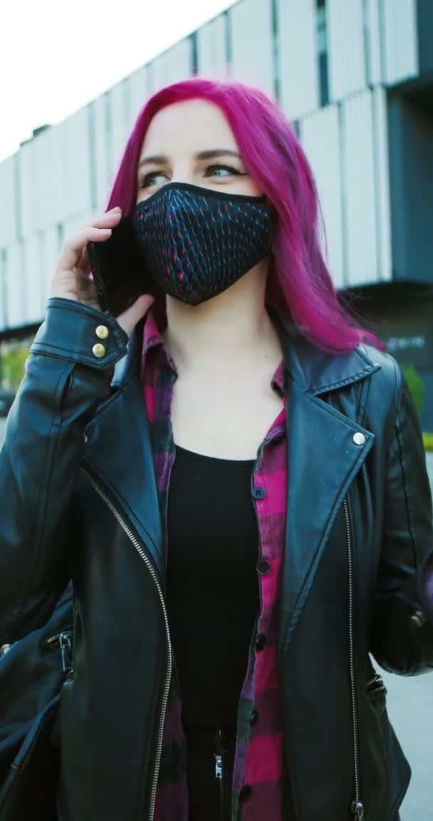 Vertical footage of young Caucasian extraordinary girl with pink hair and in mask standing outdoor and talking on cellphone. Stylish female hipster speaking on mobile phone. Video for stories. — Stock Video